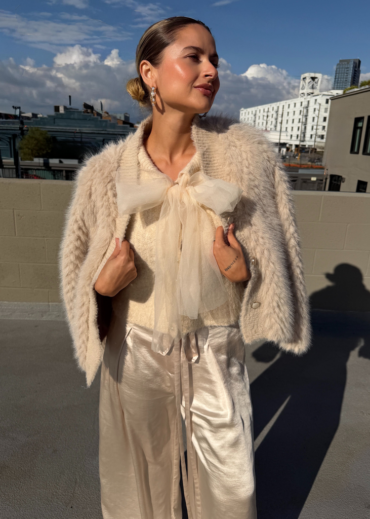 Woman in a light-colored outfit with a textured cardigan on a rooftop with buildings in the background