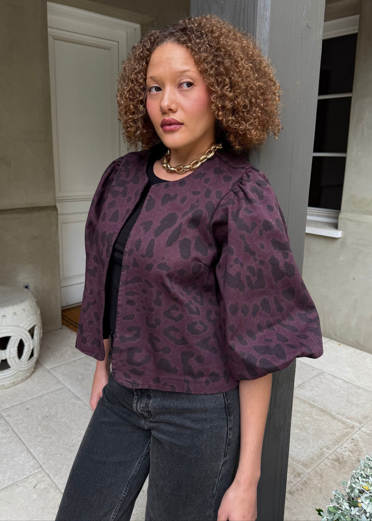 Woman wearing a purple leopard print top and dark jeans standing in an outdoor setting.