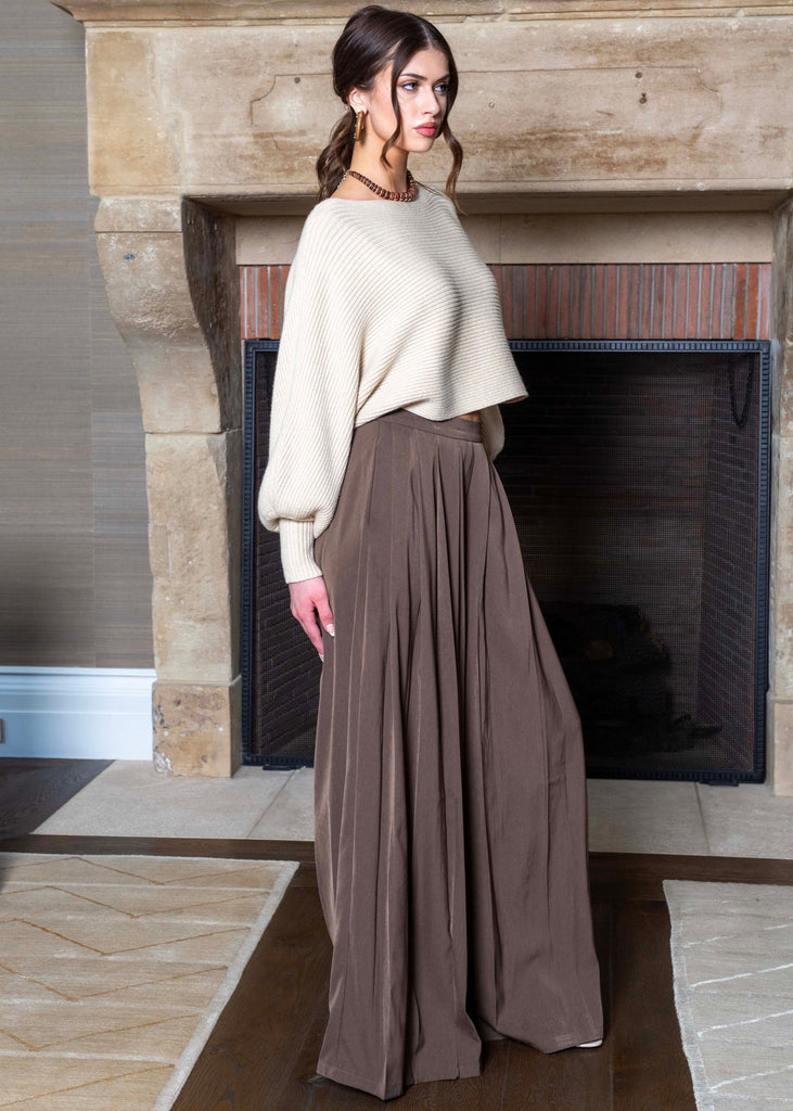 Woman in a white sweater and brown skirt standing in front of a fireplace.