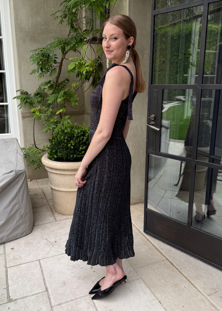 Woman in a black dress standing outdoors near a building entrance.