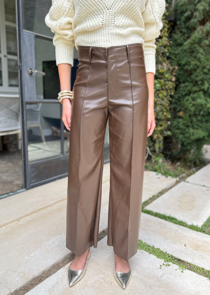 Person wearing a cream sweater and brown leather pants standing outdoors.