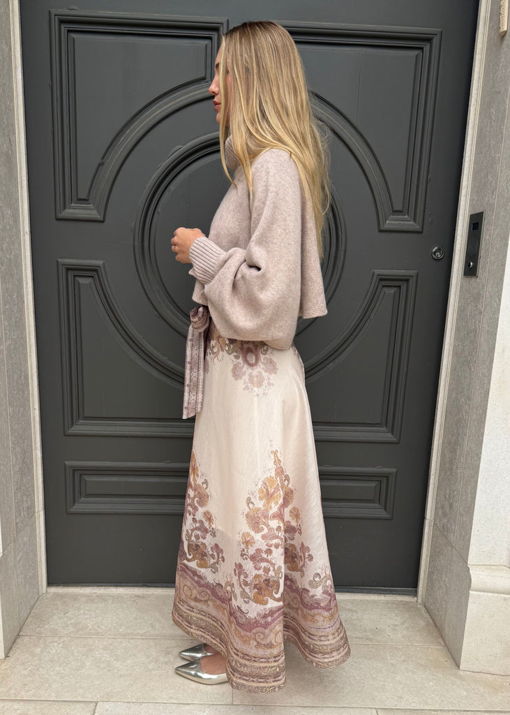 Woman in a floral dress and beige cardigan standing in front of a dark gray door.