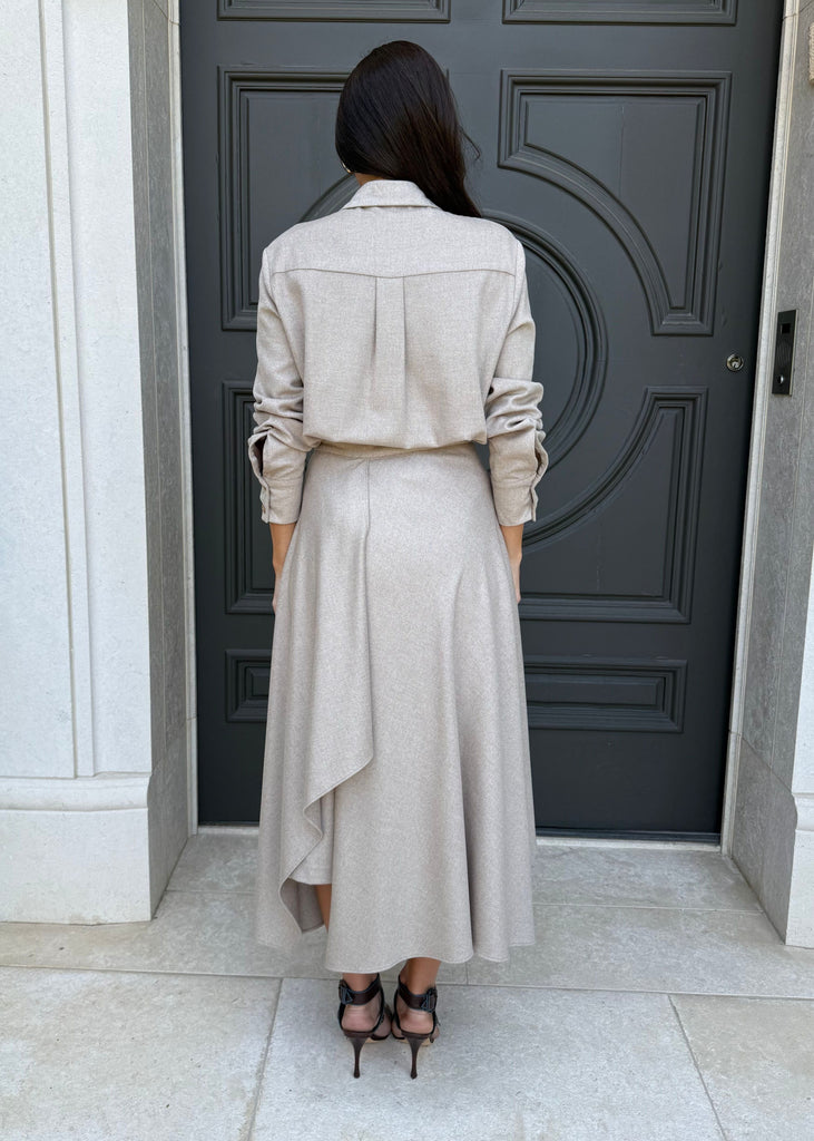 Person wearing a long beige coat standing in front of a dark door.