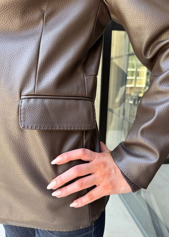 Brown leather jacket with a hand touching the fabric, blurred indoor background