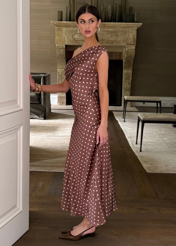 Woman in a patterned dress standing in a doorway of a stylish room with a fireplace.