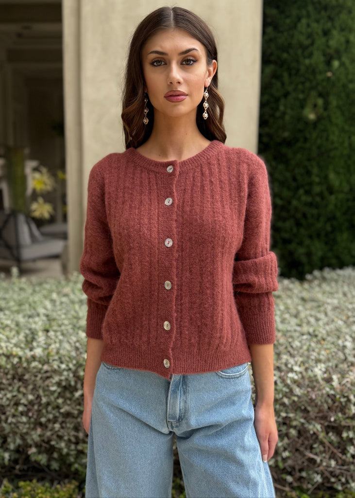 Woman wearing a red sweater and blue jeans standing outdoors.