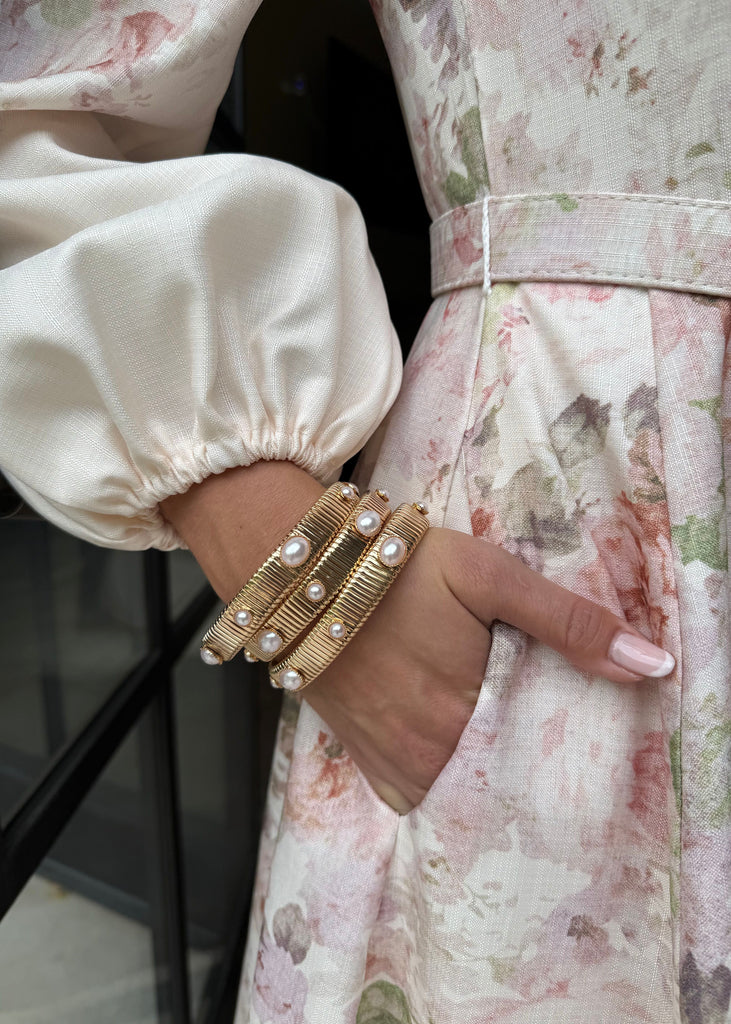 Close-up of a hand wearing gold bangles on a floral dress.