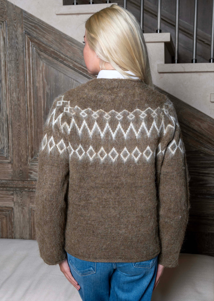 Person wearing a brown sweater with a white pattern, standing on a staircase.