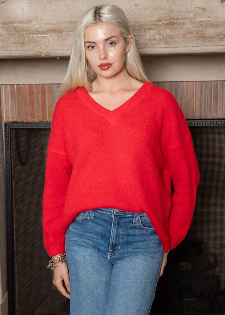 Woman wearing a red sweater and blue jeans standing in front of a wooden wall.