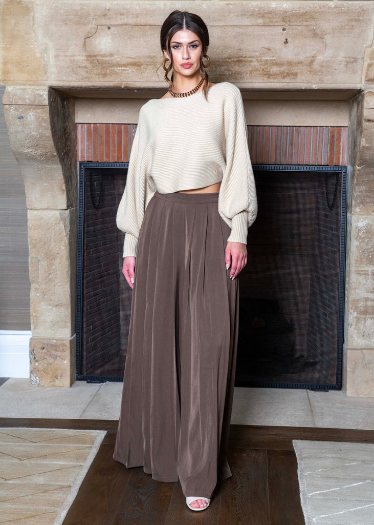Woman in a beige top and brown pants standing in front of a fireplace.