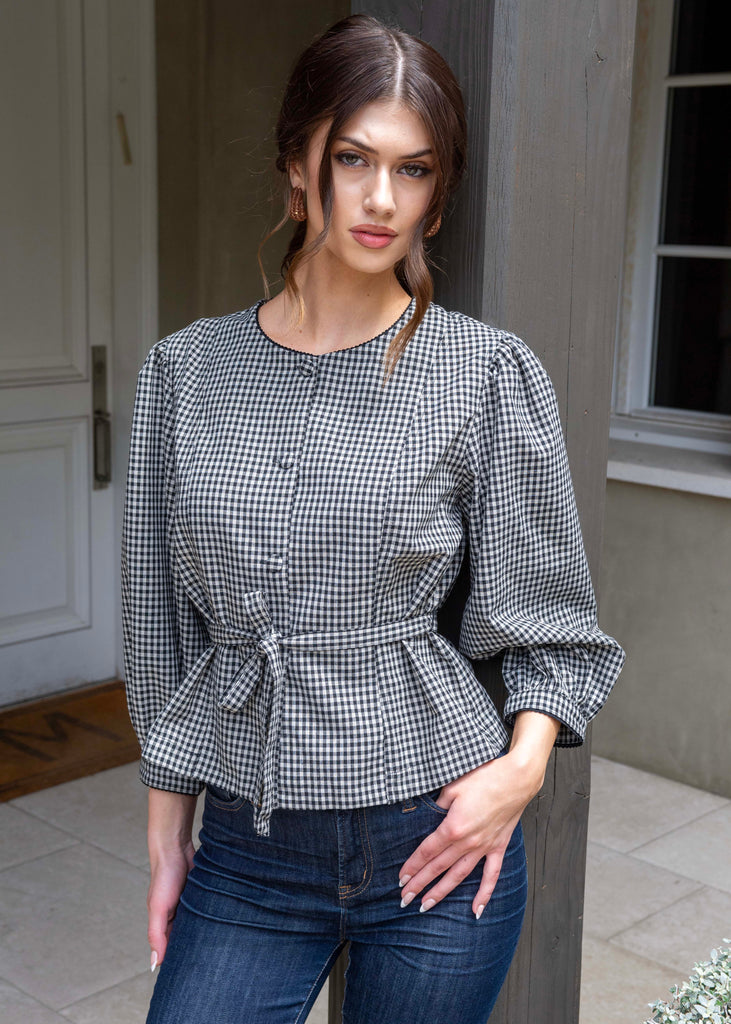 Woman wearing a black and white checkered blouse with blue jeans standing outdoors.