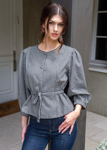 Woman wearing a black and white checkered blouse with blue jeans standing outdoors.