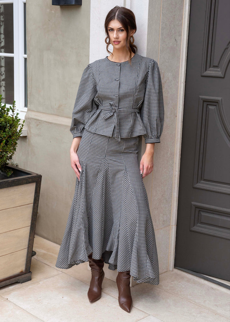 Woman in a gray checkered outfit standing in front of a door.