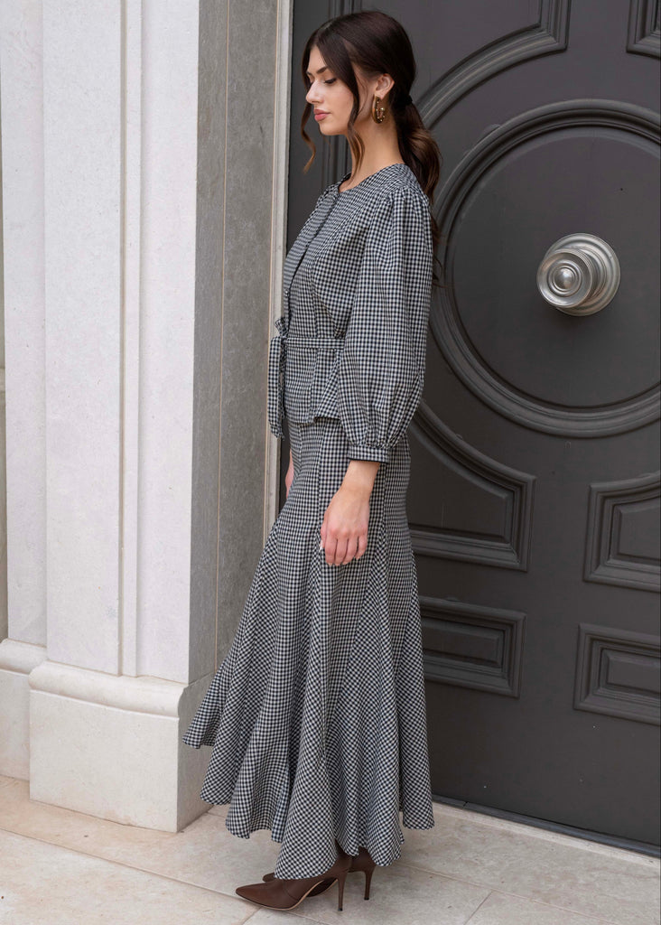 Woman in a gray checkered dress standing in front of a dark door.