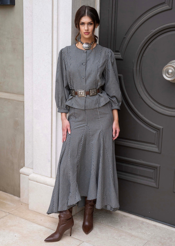 Woman in a gray checkered outfit standing in front of a dark door.