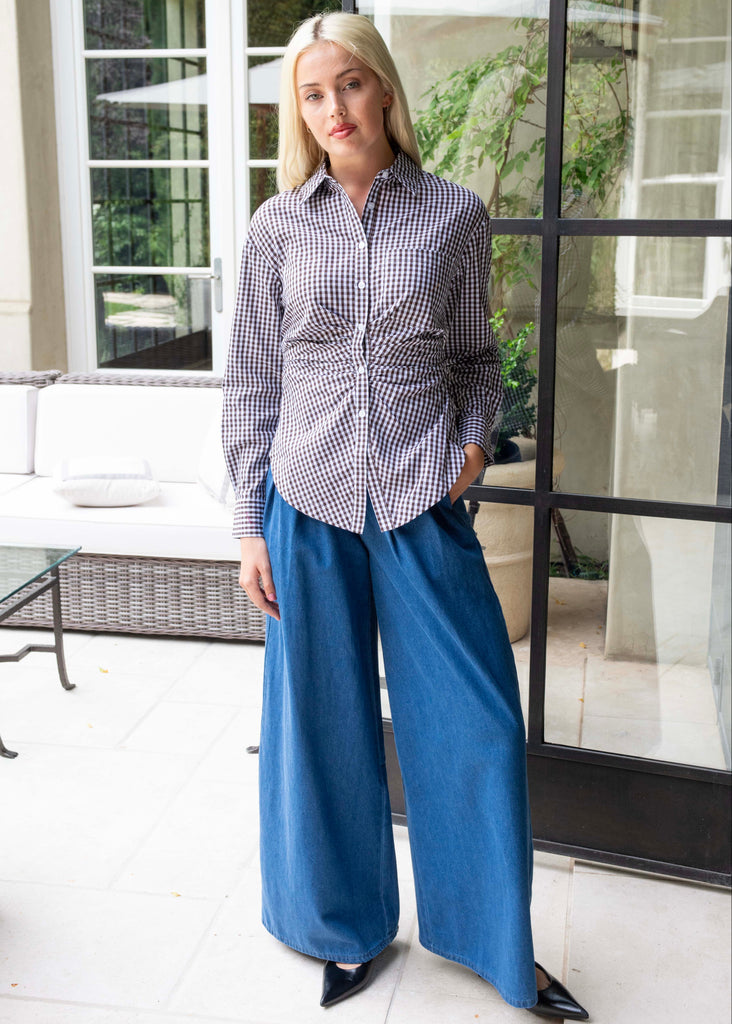 Woman wearing a checkered shirt and blue pants standing in a modern outdoor setting.