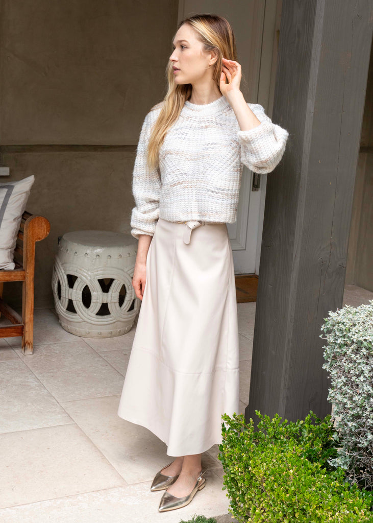 Woman in a white outfit standing outdoors near a building entrance.