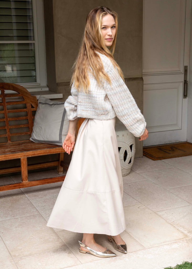 Woman in a light gray sweater and white skirt standing on a patio.