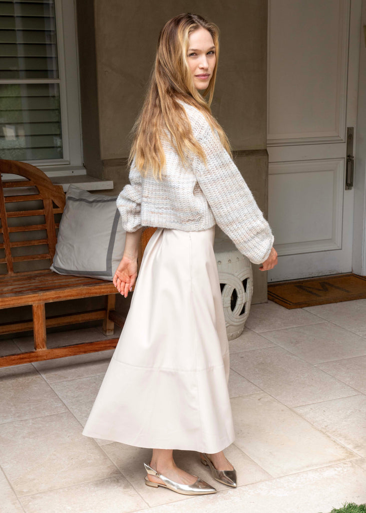 Woman in a light gray sweater and white skirt standing on a patio.