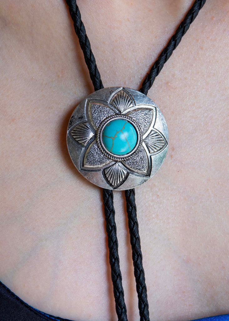 Close-up of a turquoise stone bolo tie on a person's neck with a blurred background.