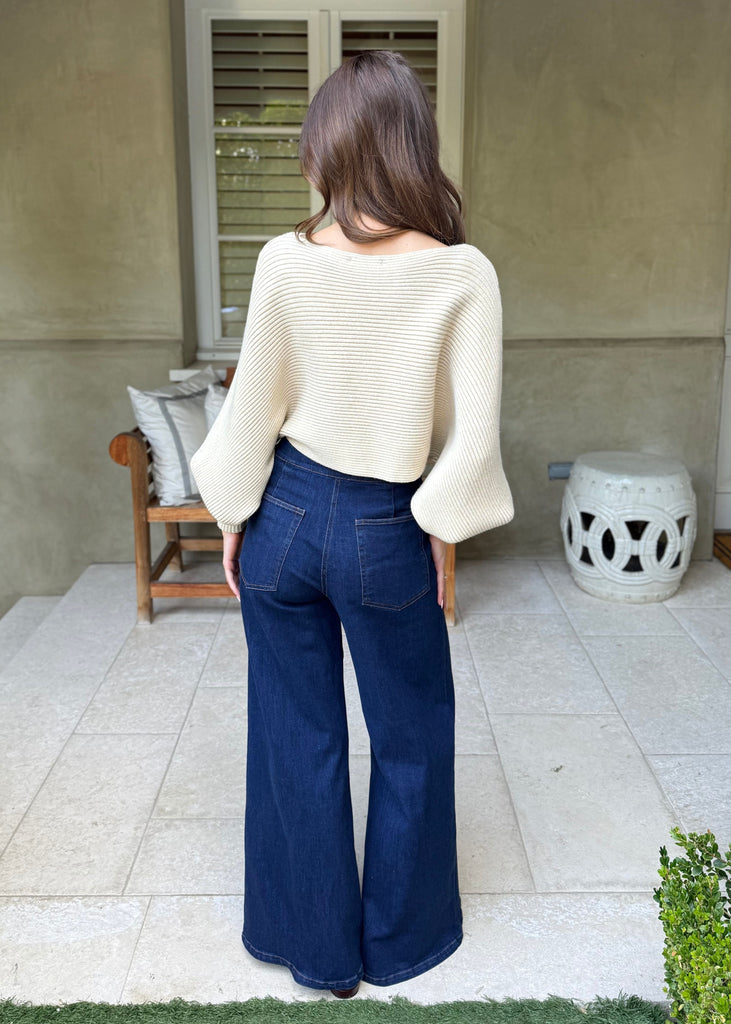 Woman wearing a white sweater and blue jeans standing on a patio.