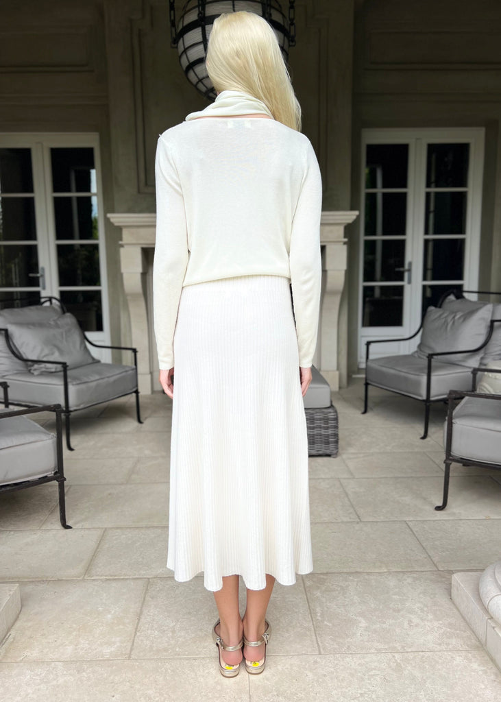 Woman in a white dress standing in a patio area with chairs and a fireplace.