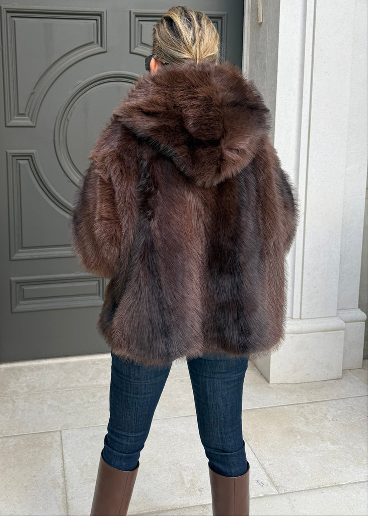 Person wearing a fur coat standing on a doormat with a door in the background