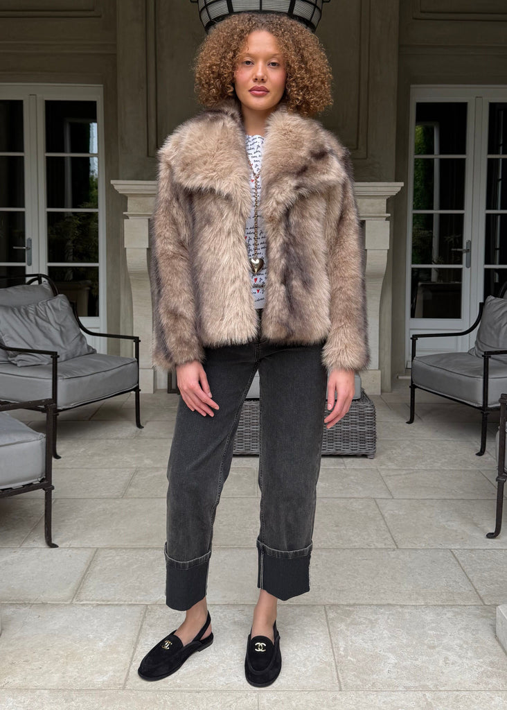 Person wearing a fur coat standing in a patio area with columns and chairs.