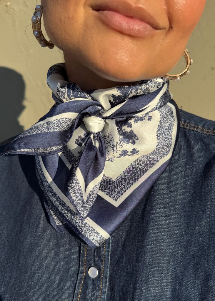 Person wearing a navy blue and white patterned scarf around their neck, with a denim shirt.