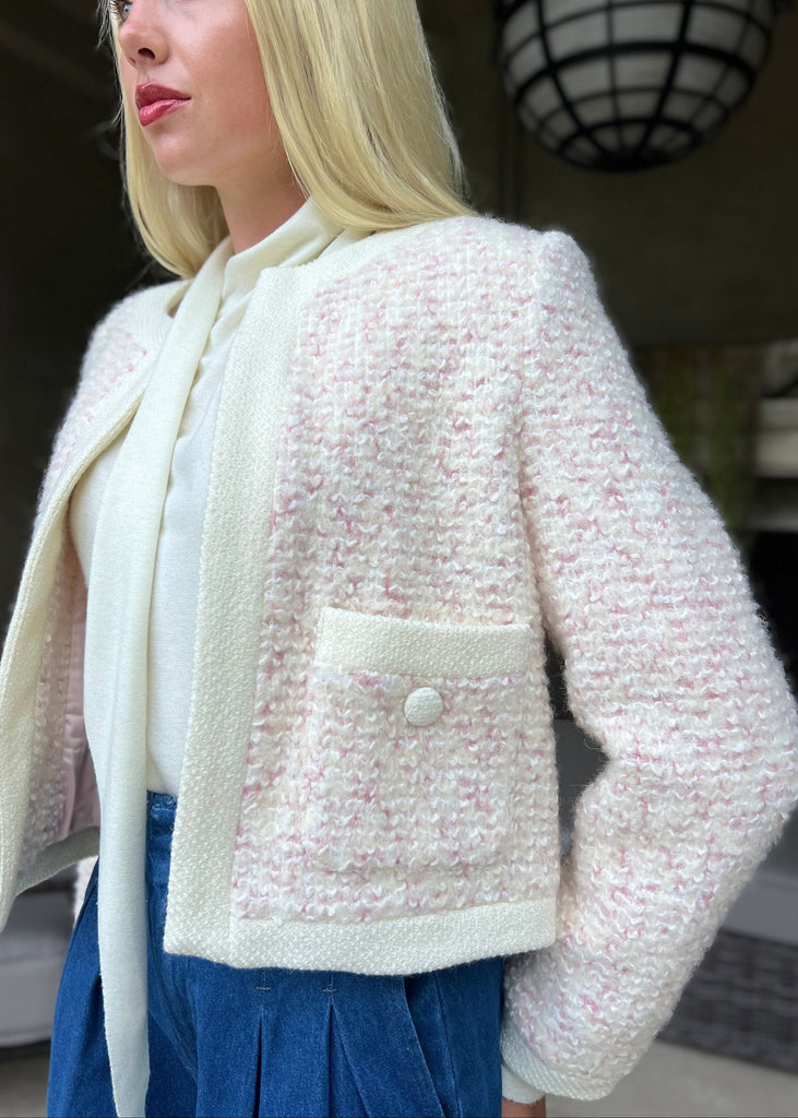 Woman wearing a textured pink and white jacket with a bow tie in an indoor setting.