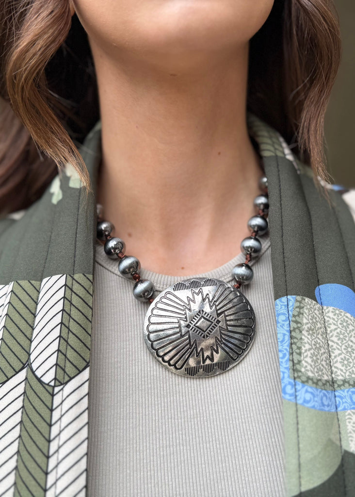 Person wearing a patterned cardigan with a necklace featuring a large pendant.