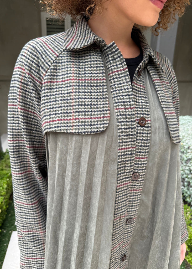Person wearing a checkered shirt over a striped shirt with a blurred outdoor background