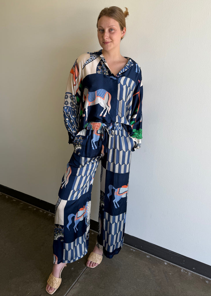 Woman wearing a patterned outfit standing against a plain wall.