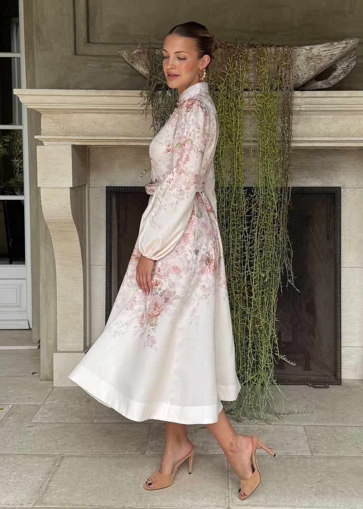 Woman in a white floral dress standing in a stylish room with a fireplace.
