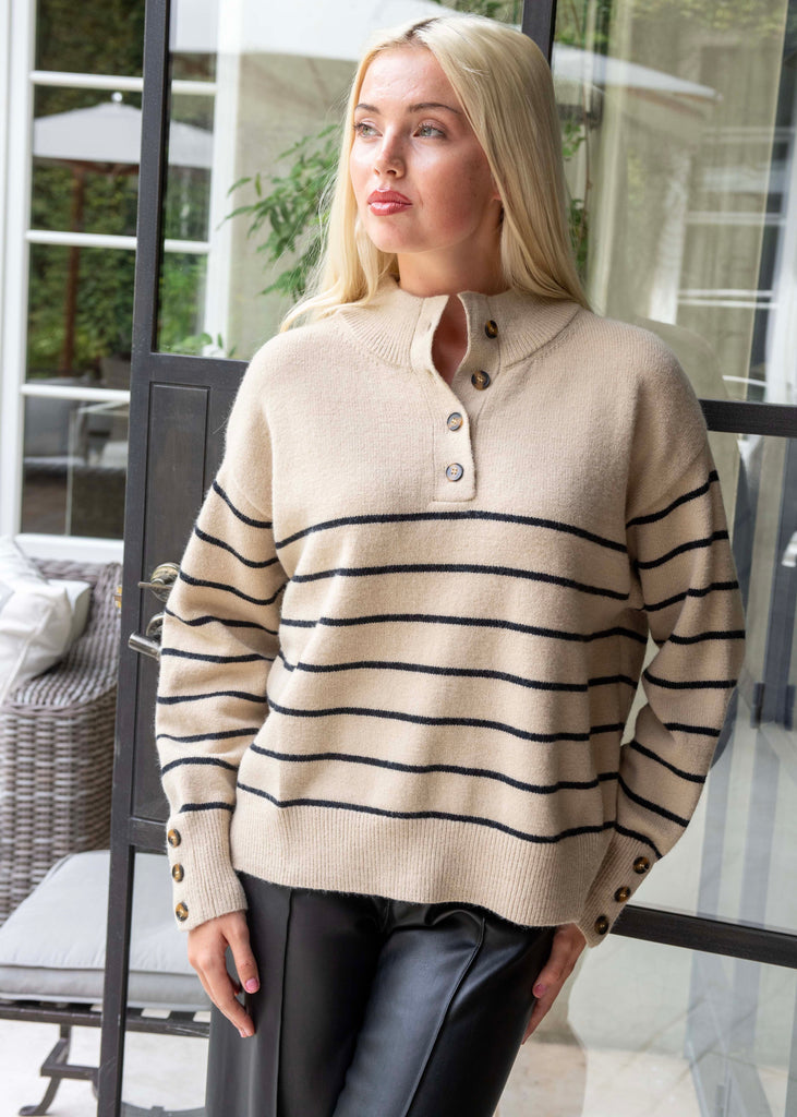 Woman wearing a beige sweater with black stripes standing outdoors.