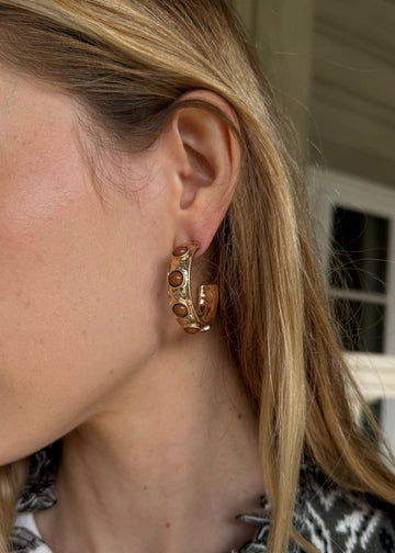Close-up of a woman wearing gold hoop earrings with a neutral background