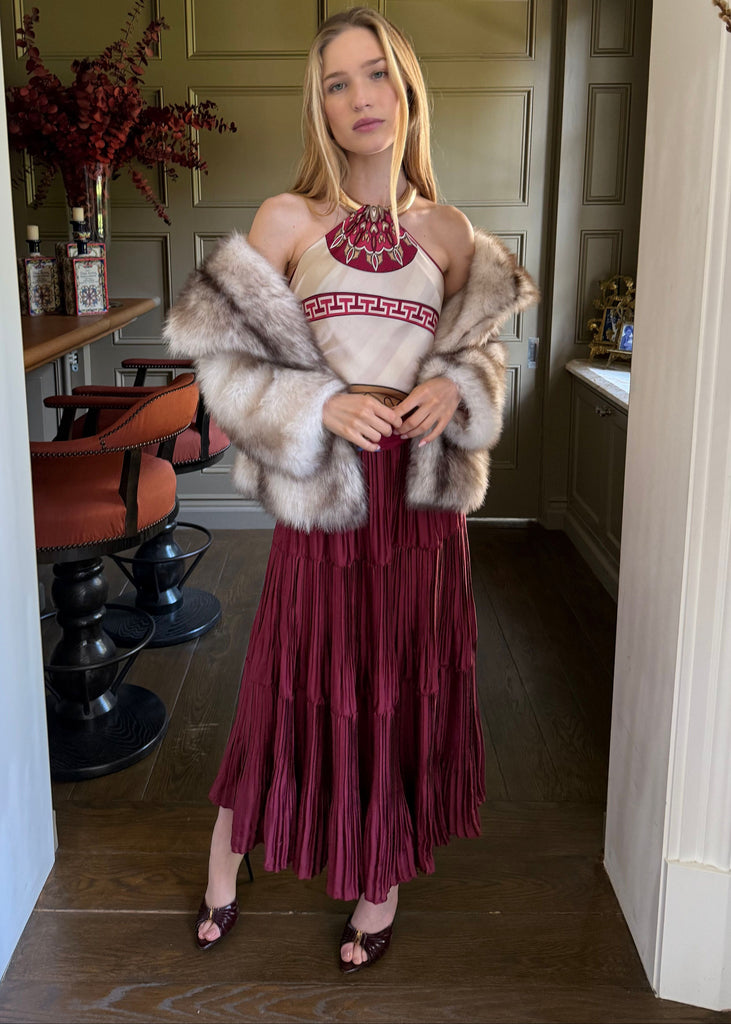 Woman in a maroon dress with a fur coat standing in a room with decor elements.