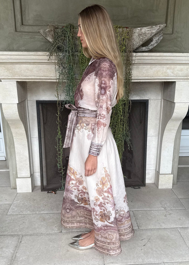Woman in a floral dress standing in front of a fireplace.