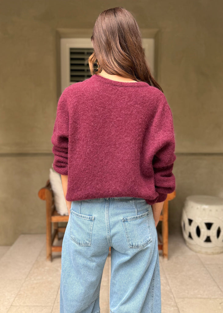Person wearing a maroon sweater and blue jeans standing in a room with a neutral color scheme.