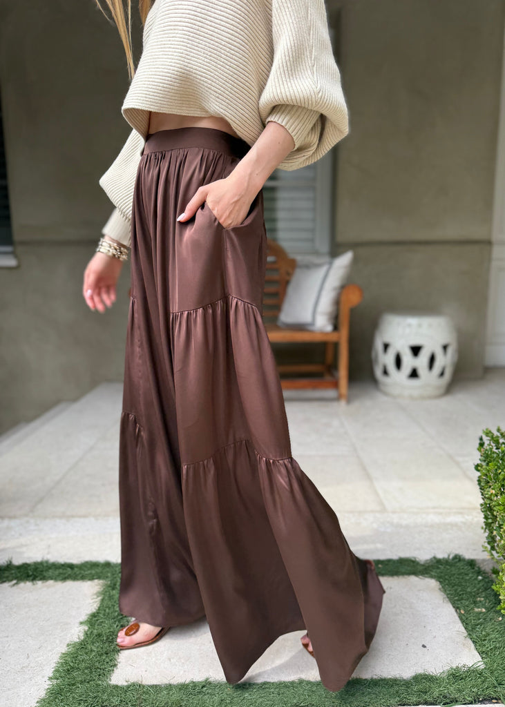 Person wearing a beige sweater and brown tiered skirt standing on a patio.