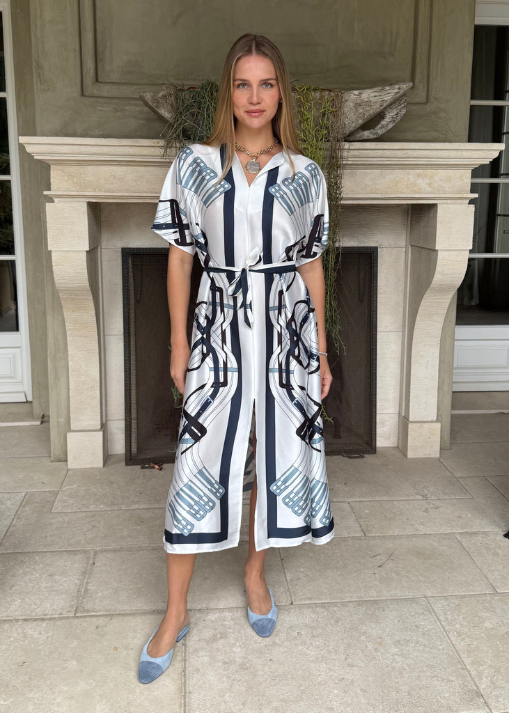 Woman in a patterned dress standing in front of a fireplace.
