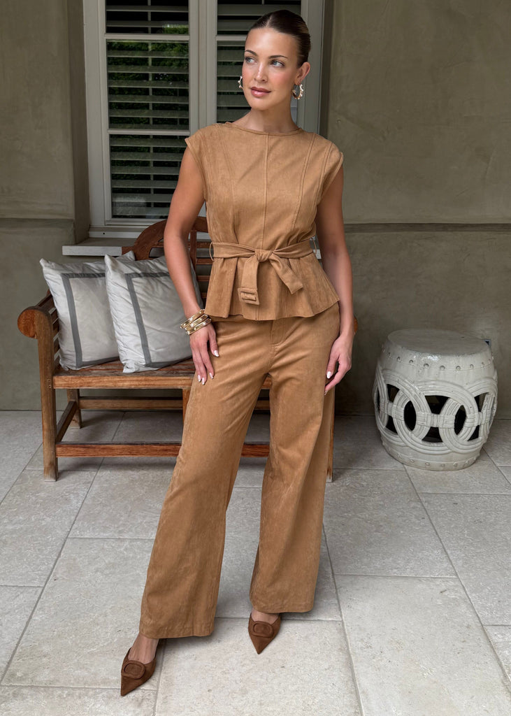 Woman in a brown outfit standing in a room with a window and bench.