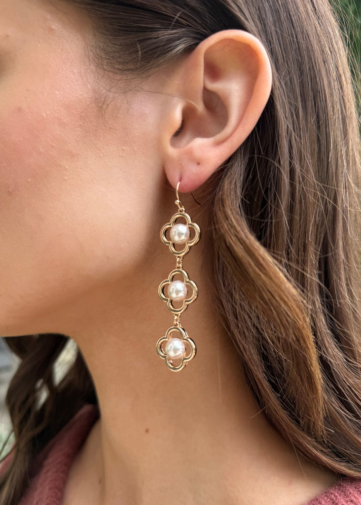 Close-up of a woman wearing gold earrings with pearl-like stones.