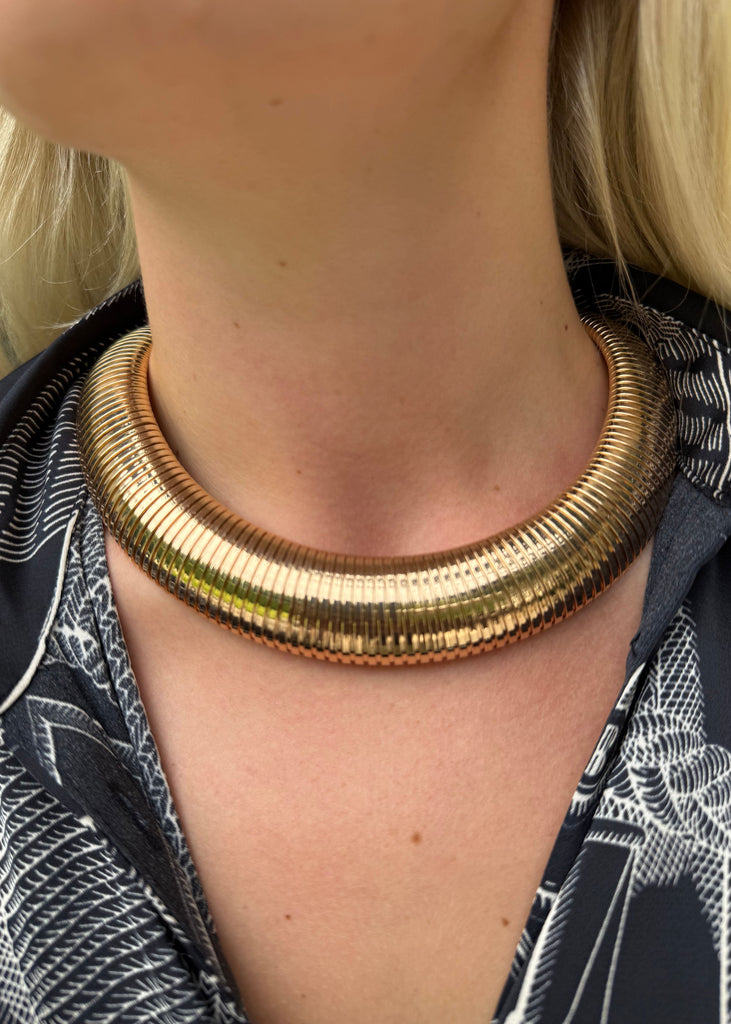 Gold necklace worn by a person with a patterned shirt