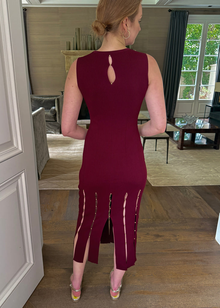 Woman wearing a burgundy dress with cut-out details in a room.