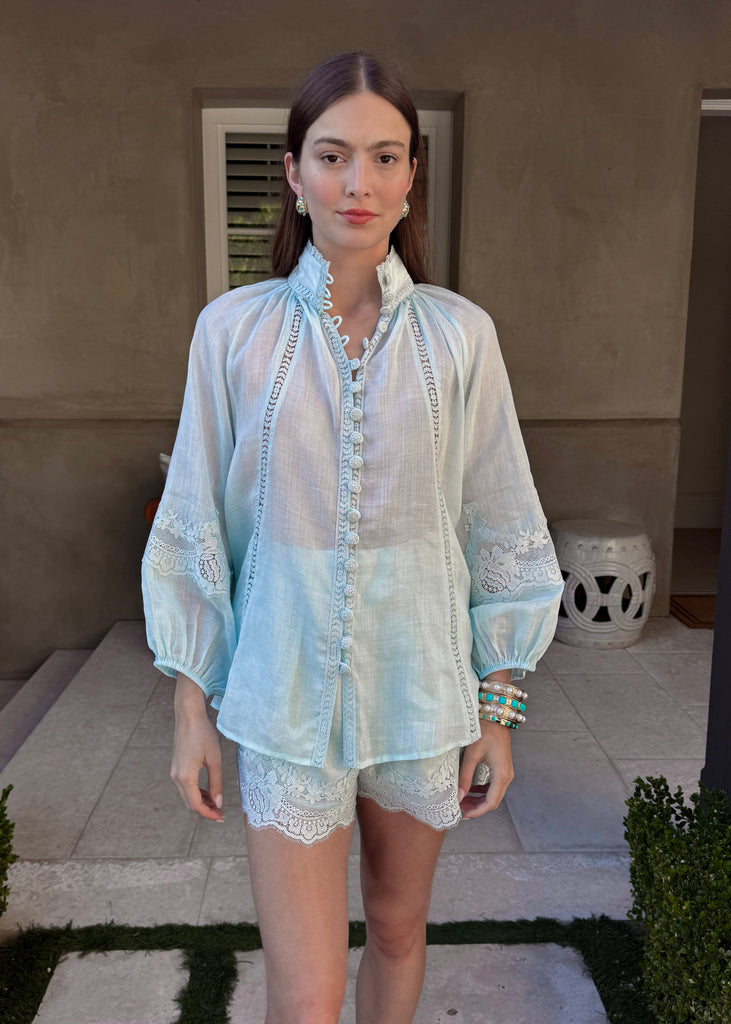 Woman wearing a light blue blouse and white shorts standing on a patio.