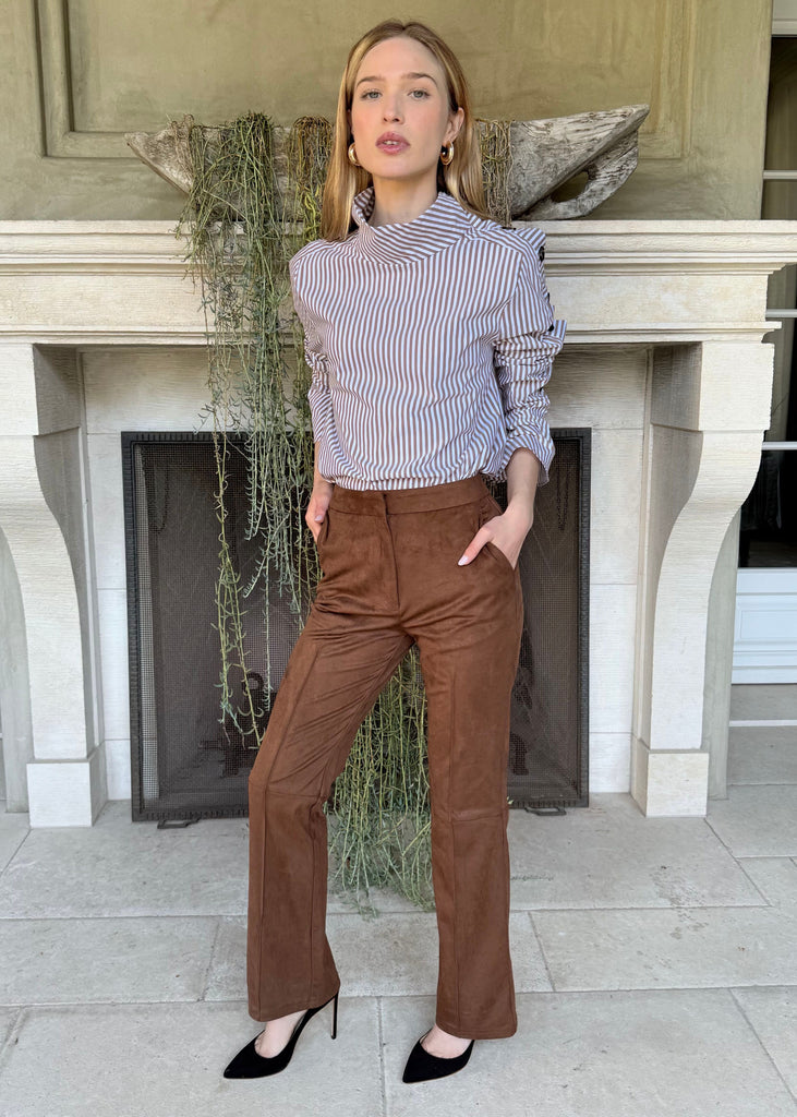 Woman standing in front of a fireplace wearing a striped shirt and brown pants.