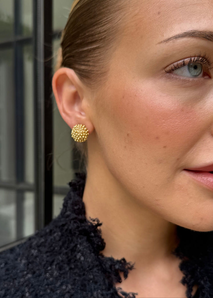 Close-up of a woman wearing gold earrings with a blurred background