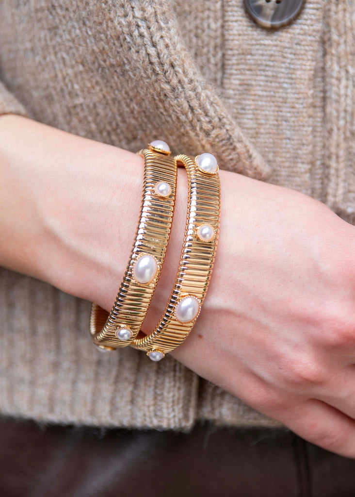 Gold bracelet with pearl-like stones on a wrist against a textured beige background