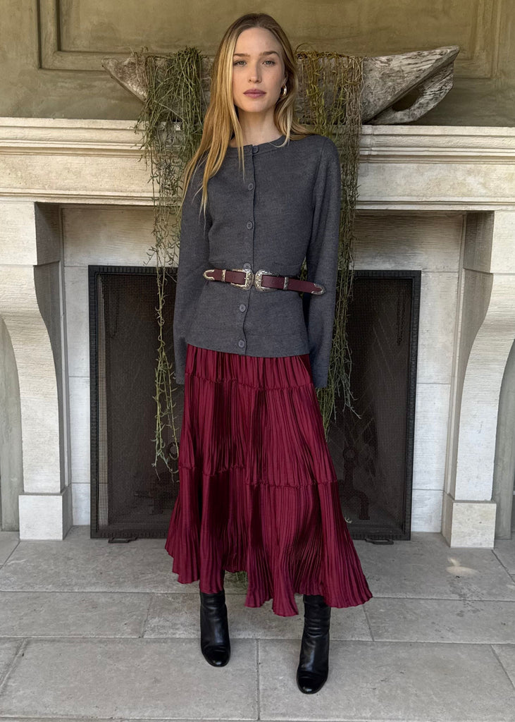 Woman in a gray top and red skirt standing in front of a fireplace.